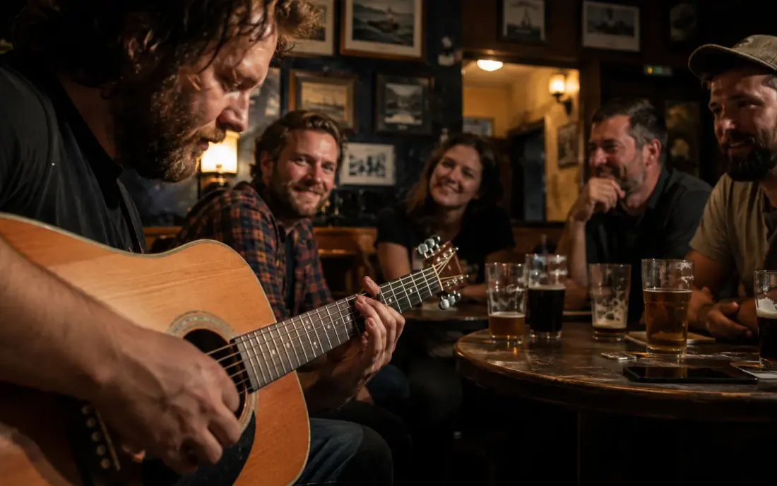 An acoustic guitarist playing a pub session to a table of regulars.