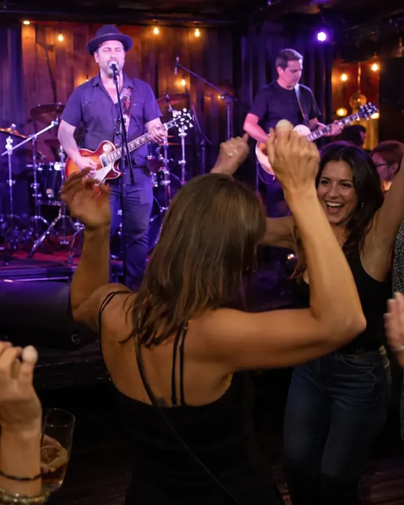 A band mid-set in a warm room, the crowd dancing right up to the stage.