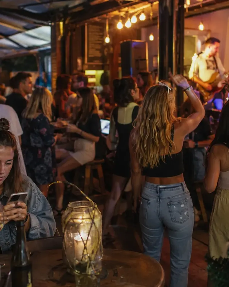 A packed terrace venue on a summer night, band on stage, every table full.