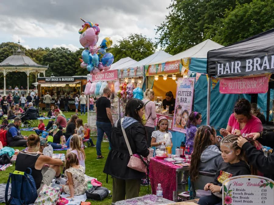 A hair-braiding and glitter stall busy with families on the green.